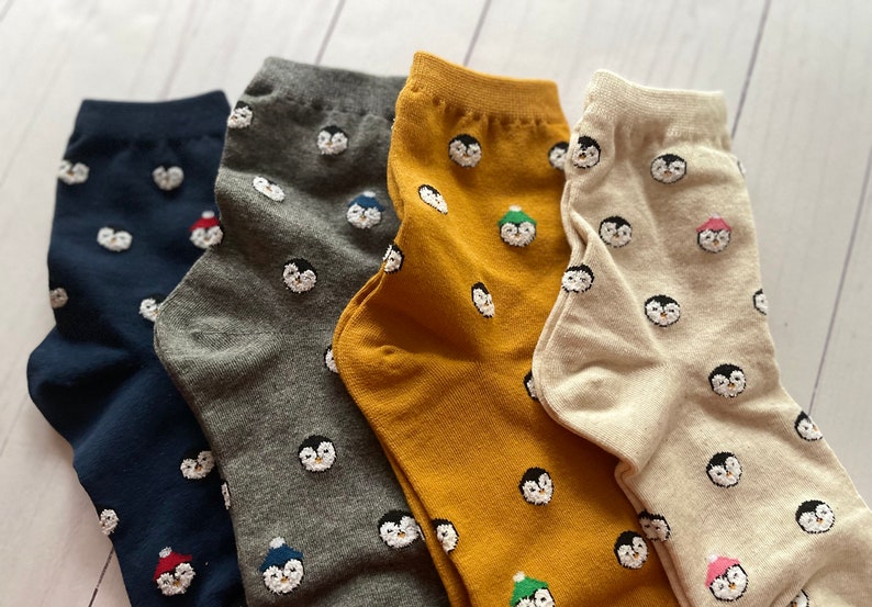 May include: Four pairs of socks with a penguin pattern. The socks are in navy blue, gray, mustard yellow, and beige.
