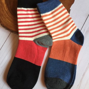 May include: A pair of colorful socks with a striped pattern. One sock features red and black sections with white and red stripes. The other sock has orange and blue sections with white and orange stripes. The socks have gray heels and toes.