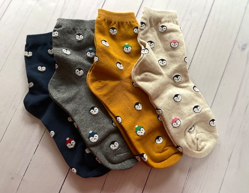 May include: Four pairs of ankle socks with a penguin pattern. The socks are in navy blue, gray, mustard yellow, and beige.