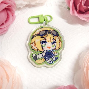 May include: A clear acrylic keychain featuring a cartoon character with blonde hair, goggles, and a blue outfit. The keychain has a green clasp and a glittery border. The background includes pink roses.