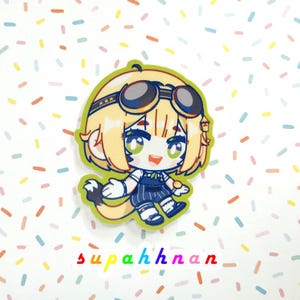 May include: A cartoon sticker featuring a character with blonde hair, green eyes, and goggles. The character is wearing a blue outfit and has a tail. The sticker is outlined in green and has the text "supahhnan" in colorful letters at the bottom.
