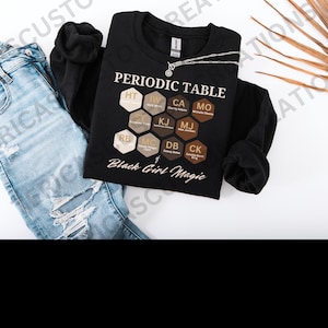 May include: Black sweatshirt with a graphic of a periodic table featuring the names of notable Black women. The text "Black Girl Magic" is printed below the table.