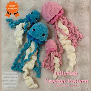 May include: Four handmade crochet jellyfish toys in varying sizes. Two are teal blue with cream-colored tentacles, and two are pink with cream-colored tentacles. Each features black safety eyes and a soft, plush yarn texture. Text on the image reads: Jellyfish Crochet Pattern by @crochetgrove.