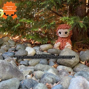 May include: A handmade crochet Bigfoot doll in shades of brown and tan sits among gray rocks and greenery. The doll has a shaggy texture and large, dark eyes. The image includes text indicating it's a crochet pattern by CrochetGrove, sold on Etsy.