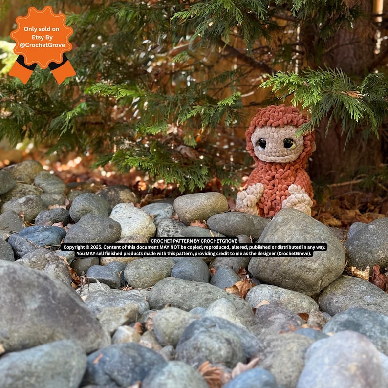 May include: A handmade crochet Bigfoot doll in shades of brown and tan sits among gray rocks and greenery. The doll has a shaggy texture and large, dark eyes. The image includes text indicating it's a crochet pattern by CrochetGrove, sold on Etsy.