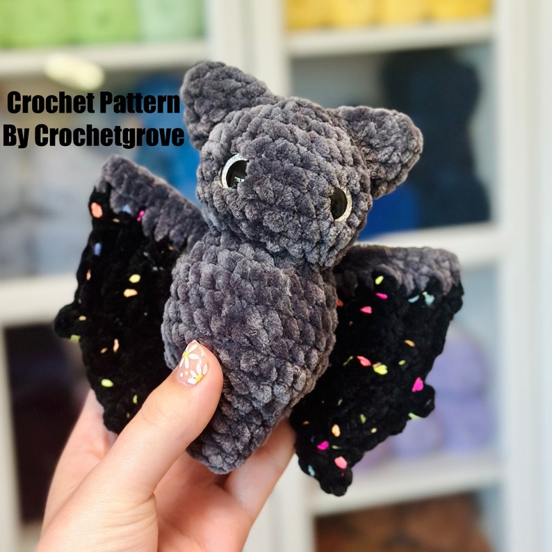Puede incluir: Un juguete de peluche de murci&eacute;lago amigurumi tejido a crochet con hilo negro y gris. El murci&eacute;lago tiene un ala moteada de negro y gris y un cuerpo gris con ojos negros.
