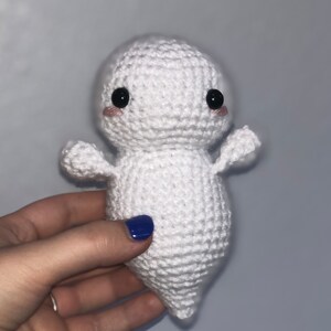 May include: White crocheted ghost plush toy with black eyes and pink cheeks. The ghost has a rounded body and small arms.