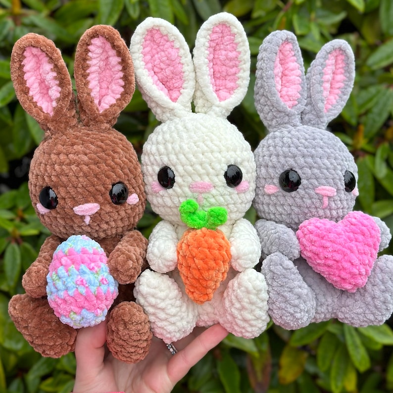 Puede incluir: Tres peluches de conejo de crochet, uno marr&oacute;n, uno blanco y uno gris. Cada conejo tiene orejas rosas y sostiene un accesorio diferente: un coraz&oacute;n rosa, una zanahoria y un huevo con estampado floral.