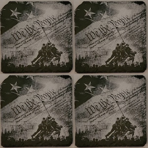 May include: Four black square coasters with a faded image of the American flag and the text "We the People" from the US Constitution. The image also includes a silhouette of four soldiers raising a flag.