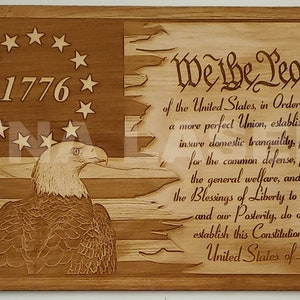 May include: Wooden plaque with an engraved design of the American flag, the text "1776", and "We the People." The design includes an eagle and the preamble to the Constitution. The plaque is made of wood.