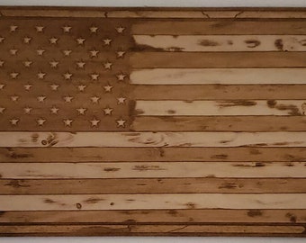 May include: A wooden American flag with a distressed, weathered look. The flag is made of individual planks of wood, giving it a rustic appearance. The stars are carved into the wood and the stripes are painted in a light brown color.