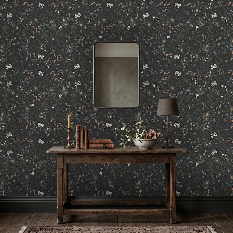 K&ouml;nnte beinhalten: Dunkle florale Tapete mit einem sich wiederholenden Muster aus kleinen wei&szlig;en, blauen und braunen Blumen und Bl&auml;ttern. Ein Holztisch tr&auml;gt B&uuml;cher, eine Lampe, eine Kerze und eine Schale mit Blumen. Ein Spiegel h&auml;ngt an der Wand &uuml;ber dem Tisch.