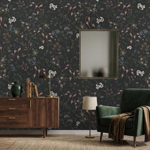 K&ouml;nnte beinhalten: Dunkle florale Tapete mit einem sich wiederholenden Muster aus Bl&auml;ttern und Blumen in Gr&uuml;n, Braun und Wei&szlig; auf schwarzem Hintergrund. Ein Holzschrank, ein gr&uuml;ner Sessel und ein Spiegel sind im Raum zu sehen.