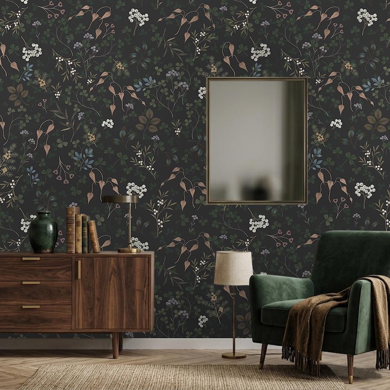 K&ouml;nnte beinhalten: Dunkle florale Tapete mit einem sich wiederholenden Muster aus Bl&auml;ttern und Blumen in Gr&uuml;n, Braun und Wei&szlig; auf schwarzem Hintergrund. Ein Holzschrank, ein gr&uuml;ner Sessel und ein Spiegel sind im Raum zu sehen.