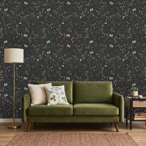 K&ouml;nnte beinhalten: Dunkle Blumentapete mit einem dichten Muster aus kleinen wei&szlig;en, blauen und braunen Blumen und Bl&auml;ttern. Vor der Tapete steht ein gr&uuml;nes Sofa mit zwei Kissen. Eine Stehlampe und ein Beistelltisch vervollst&auml;ndigen den Raum.