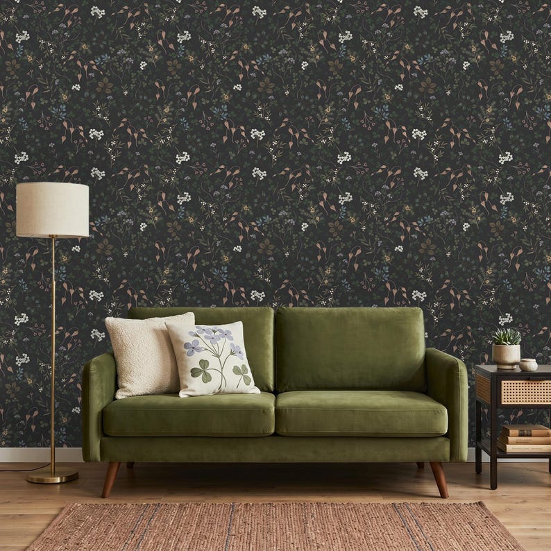 K&ouml;nnte beinhalten: Dunkle Blumentapete mit einem dichten Muster aus kleinen wei&szlig;en, blauen und braunen Blumen und Bl&auml;ttern. Vor der Tapete steht ein gr&uuml;nes Sofa mit zwei Kissen. Eine Stehlampe und ein Beistelltisch vervollst&auml;ndigen den Raum.