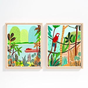 May include: Two framed art prints with a jungle theme. One print depicts a river scene with a boat, the other features a red parrot perched on a branch. Both have a light blue background and are framed in natural wood.