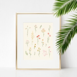 Pu&ograve; includere: Una stampa incorniciata con sfondo bianco e cornice dorata. La stampa presenta una collezione di fiori selvatici disegnati a mano in tonalit&agrave; di rosa, giallo e verde. Il testo "Stay Wild" &egrave; scritto in corsivo rosa nella parte inferiore della stampa.