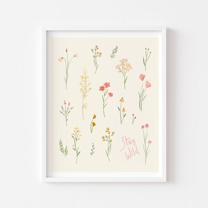 Pu&ograve; includere: Uno sfondo beige con una cornice bianca attorno a una stampa di vari fiori in tonalit&agrave; di rosa, giallo e arancione. Il testo "Stay Wild" &egrave; scritto in rosa nella parte inferiore della stampa.