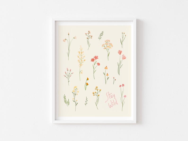 Pu&ograve; includere: Uno sfondo beige con una cornice bianca attorno a una stampa di vari fiori in tonalit&agrave; di rosa, giallo e arancione. Il testo "Stay Wild" &egrave; scritto in rosa nella parte inferiore della stampa.