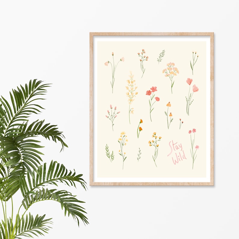 Pu&ograve; includere: Una stampa incorniciata con sfondo crema che presenta una collezione di fiori selvatici disegnati a mano in tonalit&agrave; rosa, arancio e giallo. Il testo "Stay Wild" &egrave; scritto in corsivo rosa nella parte inferiore della stampa.