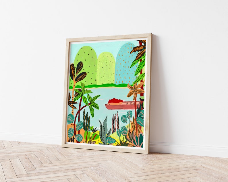 May include: A framed art print depicting a tropical landscape with a boat on the water. The artwork features green hills, palm trees, and various plants in vibrant colors. The frame is made of light-colored wood.