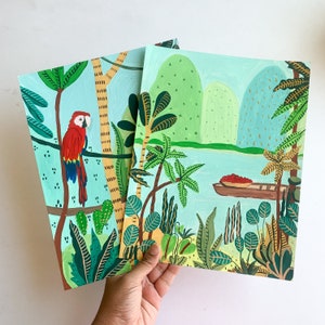 May include: Two colorful acrylic paintings featuring tropical scenes. One depicts a red macaw perched on a branch, the other a river scene with a boat. Both paintings have a light blue background and lush green foliage.