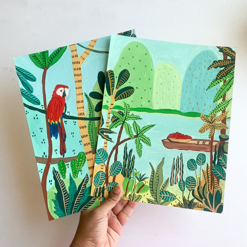 May include: Two colorful acrylic paintings featuring tropical scenes. One depicts a red macaw perched on a branch, the other a river scene with a boat. Both paintings have a light blue background and lush green foliage.