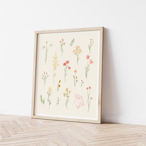 Pu&ograve; includere: Una stampa incorniciata con uno sfondo beige che presenta una collezione di fiori selvatici disegnati a mano in tonalit&agrave; di rosa, giallo e verde. Il testo "Stay Wild" &egrave; scritto in rosa nella parte inferiore della stampa.