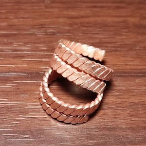 May include: Three copper rings with a braided design. The rings are stacked on top of each other.