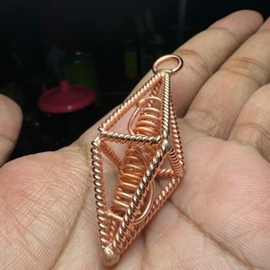 May include: A copper wire cage pendant with a spiral inside. The cage is in the shape of a pyramid with a rounded top.