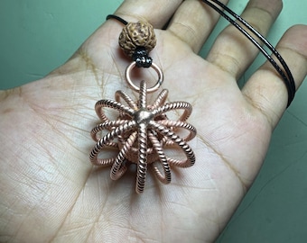 May include: A copper-colored pendant necklace featuring a spherical, openwork design. The pendant is suspended from a black cord and includes a natural-looking bead at the top. The intricate metalwork creates a unique, eye-catching accessory.
