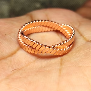 May include: A copper ring with a braided design. The ring is made of two strands of copper wire that are twisted together.