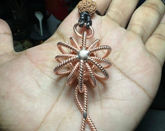 May include: A copper wire pendant with a star-shaped design and a knotted loop at the bottom. The pendant is attached to a black cord with a brown wooden bead.