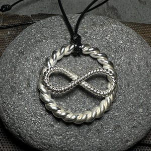 May include: A silver infinity symbol pendant necklace with a twisted rope design. The necklace is on a black cord.
