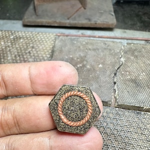 Op de afbeelding: Een zeshoekige harscabochon met een ontwerp van koperdraadtouw. De cabochon heeft een zwarte en gouden glitterachtergrond.