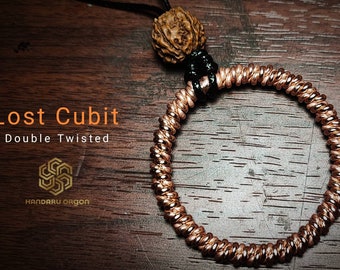 May include: A copper double twisted bracelet with a black cord and a brown wooden bead. The bracelet is on a wooden surface. The text "Lost Cubit Double Twisted" and "Handaru Orgon" is visible on the image.