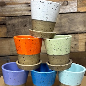 May include: Six ceramic planters with speckled glaze in various colors, including white, orange, green, purple, blue, and light blue. Each planter has a matching saucer.