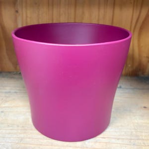 May include: A deep magenta colored plastic plant pot. The pot is round and has a slightly flared lip.