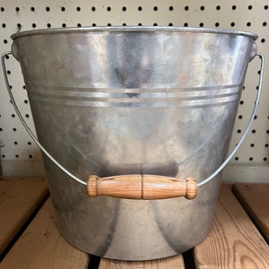 May include: A silver galvanized metal bucket with a wooden handle. The bucket is empty and has a slightly distressed look.