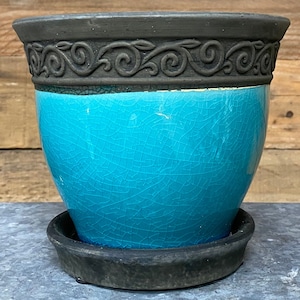 May include: A turquoise ceramic planter with a decorative black rim and a matching saucer. The planter has a crackled glaze finish.