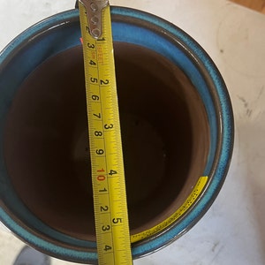 Op de afbeelding: Een blauwe en bruine keramische plantenpot met een gele meetlint ernaast. De tape meet 12,7 cm.