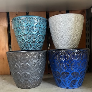 May include: Four ceramic flower pots with a decorative embossed pattern. The pots are in shades of blue, gray, and white.