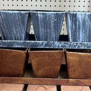 May include: Set of three gray metal planters with a distressed finish, each with a matching tray. The planters are stacked on top of each other, with the top row of planters being gray and the bottom row being brown.