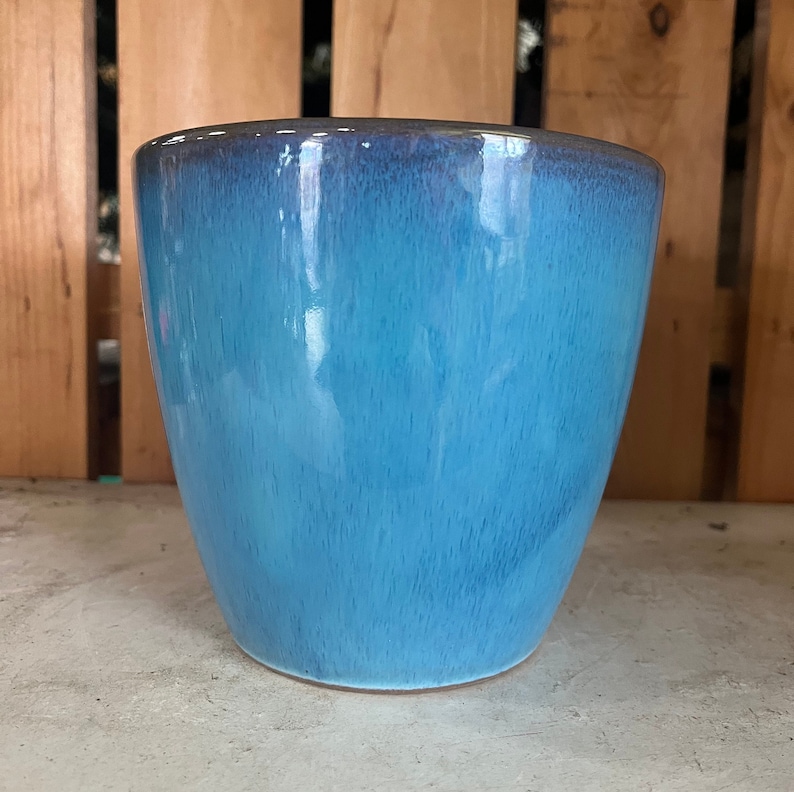 Op de afbeelding: Een blauwe keramische pot met een glanzende afwerking. De pot heeft een afgeronde vorm en een brede opening.