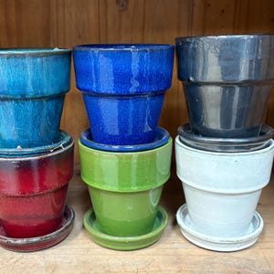 May include: Six ceramic flower pots in various colors, including blue, green, red, white, and gray. The pots are all the same size and shape, with a rounded bottom and a flared lip.