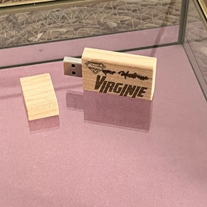 May include: A wooden USB drive with a Superman logo and the text "Super Heroine VIRGINIE" engraved on it. The drive is in a glass display case.