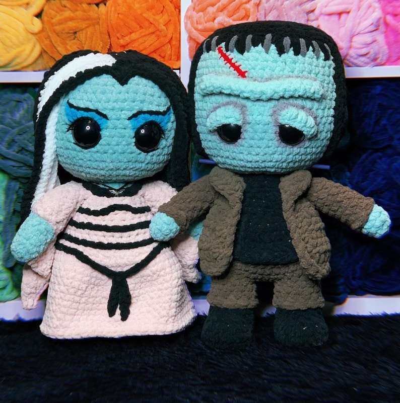 May include: A crocheted plush toy set featuring a blue and white striped dress with a pink dress and a blue and brown Frankenstein monster with a brown jacket.