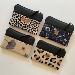 Könnte beinhalten: Vier rechteckige Reißverschlusstaschen mit einem schwarzen oberen Teil und einem gemusterten unteren Teil. Die Muster umfassen schwarz-weißes Leopardenmuster mit 'handmade FASHION'-Etikett, dunkle Blumen, Ginkgoblätter und beiges Leopardenmuster.