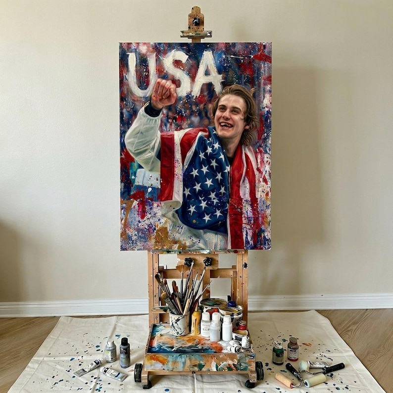 Pode incluir: Uma pintura num cavalete retrata uma pessoa envolta numa bandeira americana, com a palavra "USA" acima. A obra de arte &eacute; vibrante com cores vermelhas, brancas e azuis, e a pessoa est&aacute; sorrindo e levantando o punho.